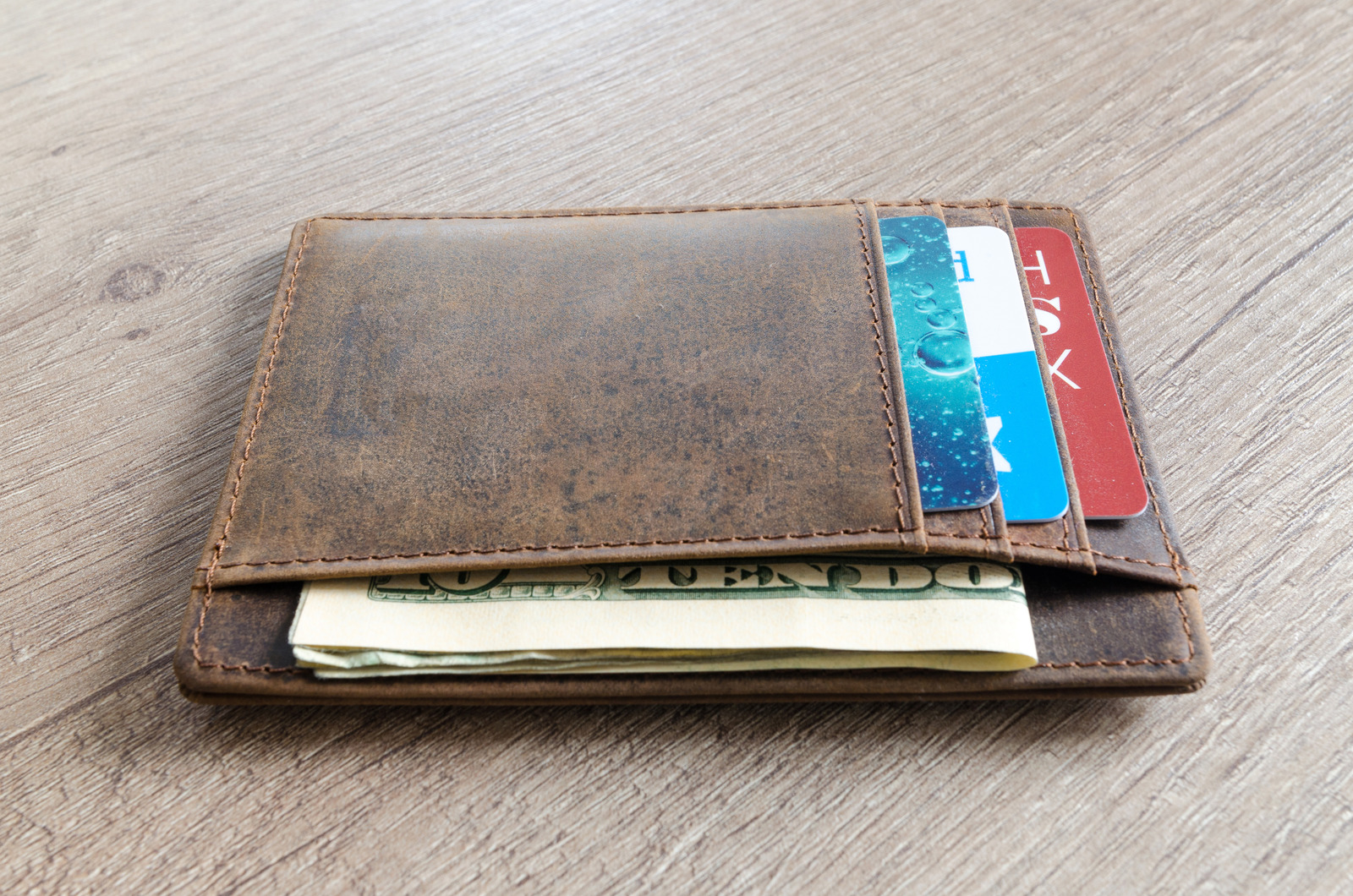 Leather wallet with cards and money inside sitting on a wooden table