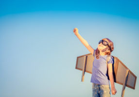 Smiling child standing with cardboard wings on back looking toward the sky